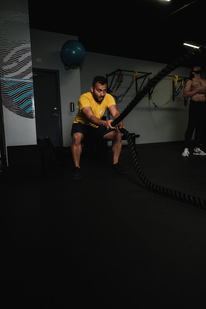 Focused man in yellow shirt working out with battle ropes in a gym setting.