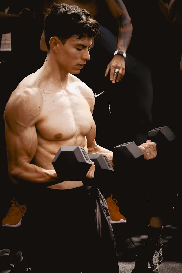 Young man training with dumbbells, showcasing strength and fitness in an indoor gym setting.