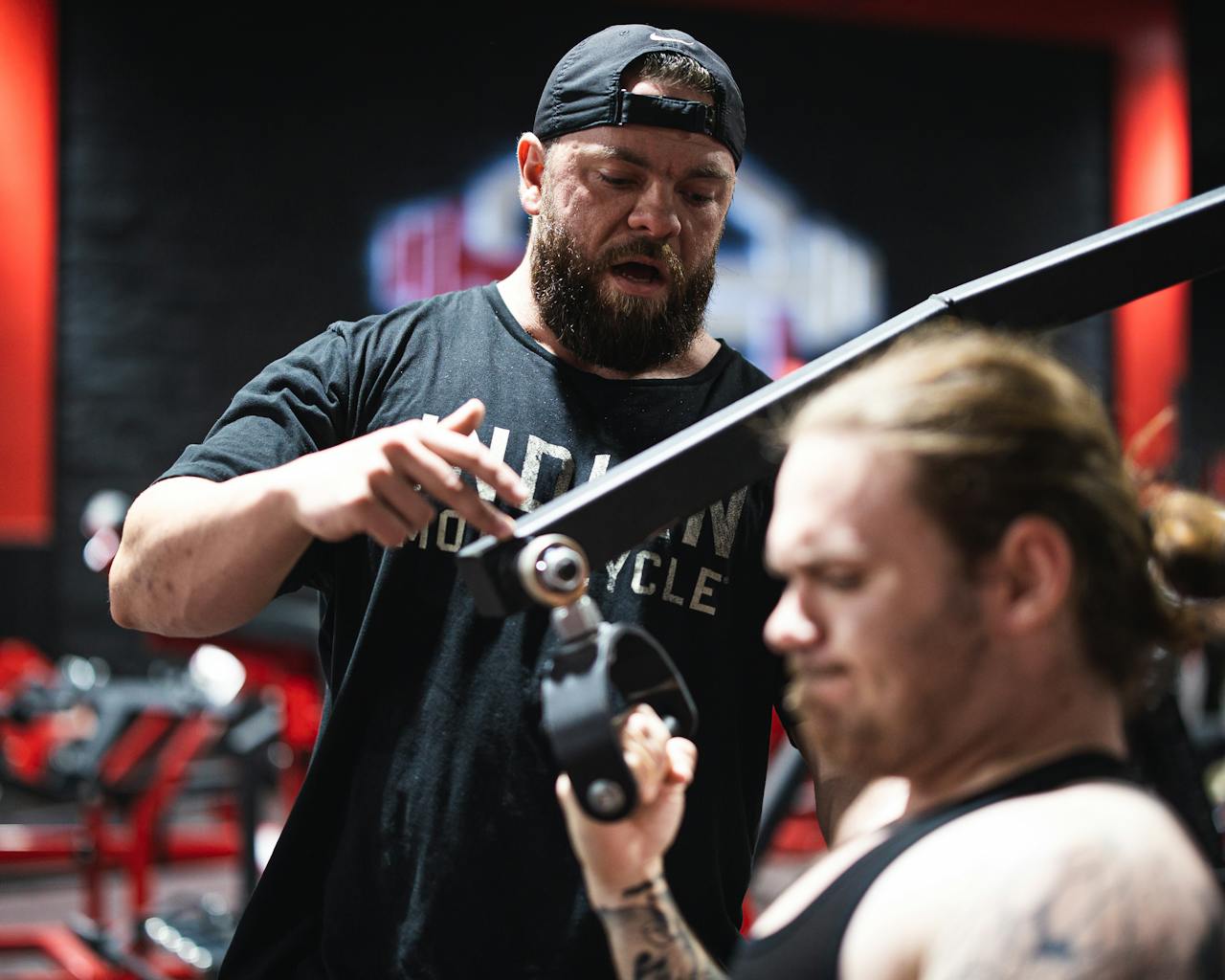 A personal trainer guides a man through an intense gym workout session, focusing on strength and technique.
