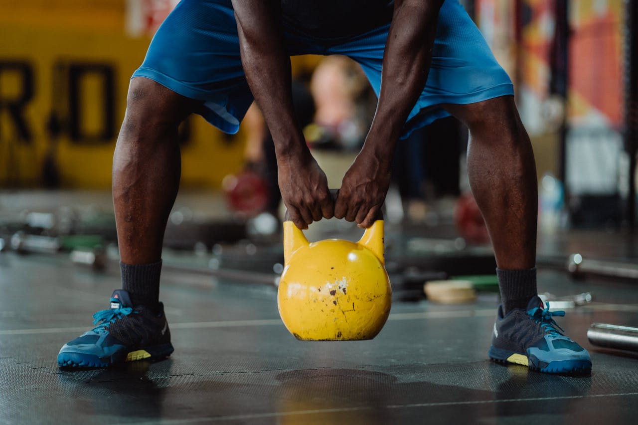Focused workout scene of athlete lifting a yellow kettlebell in the gym.