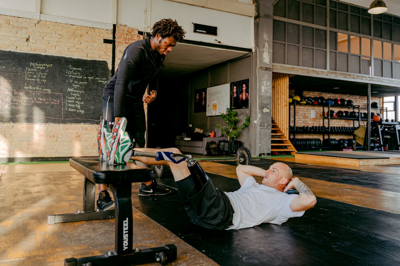 Man with prosthetic leg doing crunches in gym with personal trainer's support.